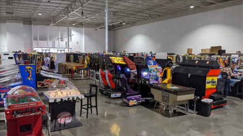 A spacious arcade filled with various vintage pinball and arcade machines, with people enjoying the games.