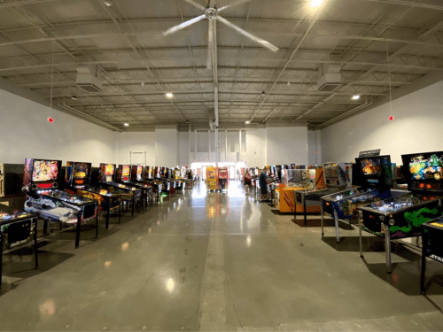 A spacious arcade filled with rows of colorful pinball machines under bright lights.