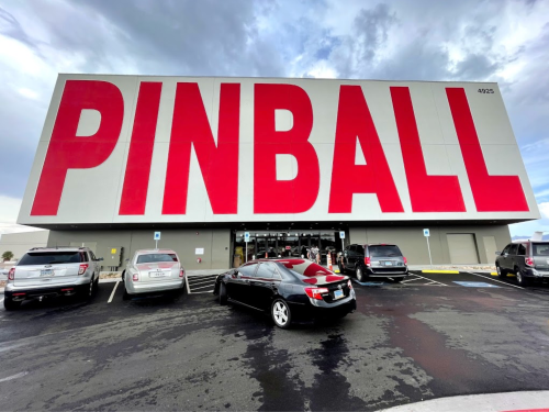 A large building with "PINBALL" in bold red letters on the facade, surrounded by parked cars.