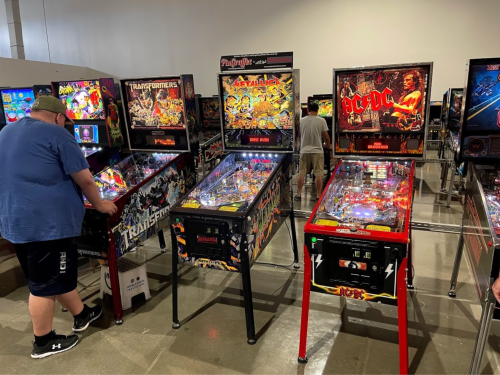 A person plays a pinball machine at an arcade, surrounded by various themed pinball games.
