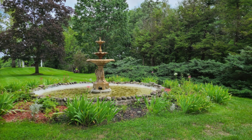 A serene garden scene featuring a central fountain surrounded by lush greenery and colorful flowers.