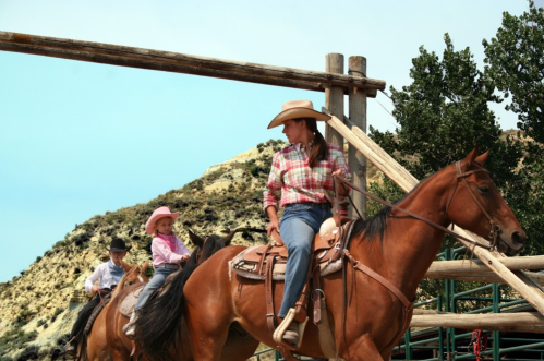 A woman and a child ride horses, while a man on horseback follows them in a scenic outdoor setting.