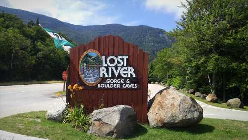 Sign for Lost River Gorge and Boulder Caves, surrounded by greenery and mountains under a clear blue sky.