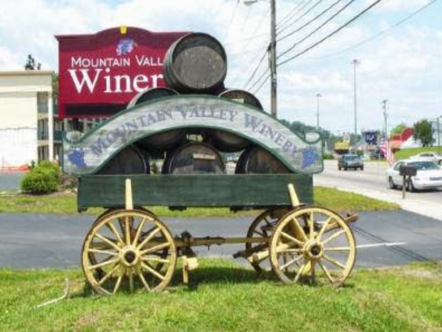 Sign for Mountain Valley Winery featuring a wagon with barrels, set against a blue sky and roadside scenery.