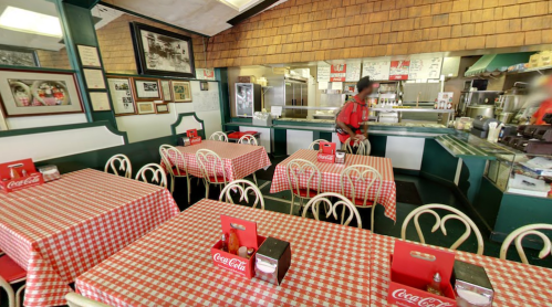 A cozy diner with checkered tablecloths, Coca-Cola decor, and a counter in the background. Staff member is serving.