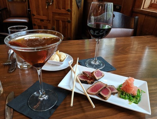 A martini and a glass of red wine beside a plate of seared tuna, garnished with wasabi and pickled ginger.