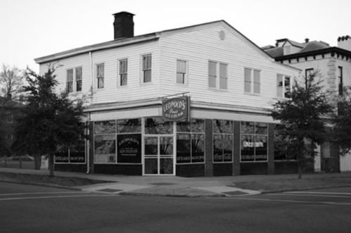 Black and white image of a corner restaurant building with large windows and a sign reading "Leopold's Ice Cream."
