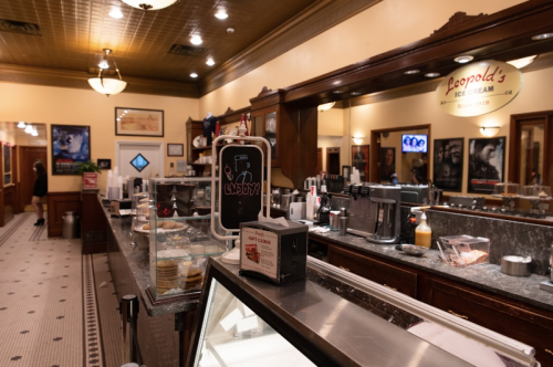 A vintage ice cream parlor with a marble counter, display cases, and nostalgic decor, featuring various ice cream toppings.