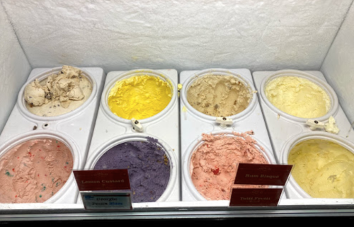 A display of eight ice cream flavors in tubs, including lemon custard, banana rum, and purple grape.
