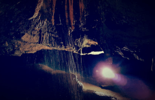 A dimly lit cave with water dripping from the ceiling, illuminated by a soft light in the background.