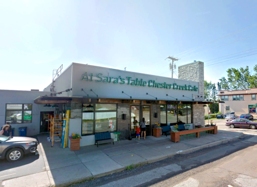 Exterior of "At Sara's Table Chester Creek Cafe," featuring a modern design and outdoor seating.