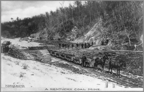 Black and white photo of a Kentucky coal mine with workers and horse-drawn carts on a snowy landscape.