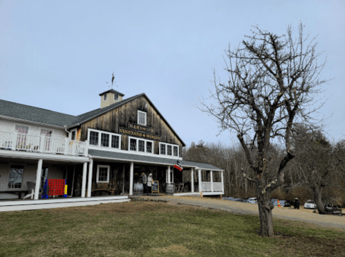 A rustic building with a wooden facade, surrounded by trees and a gravel path, on a cloudy day.