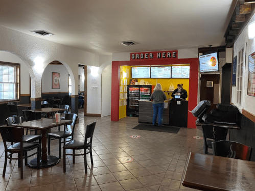 A cozy restaurant interior with tables, a counter for ordering, and a customer at the register.