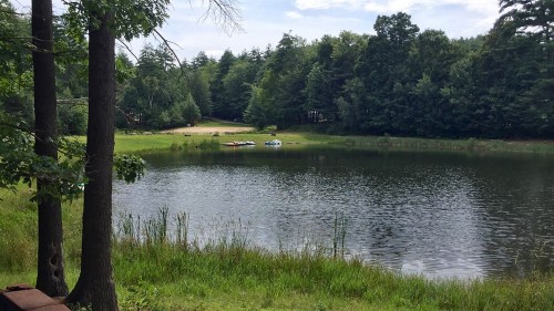 A serene lake surrounded by trees, with a small beach area and kayaks visible on the water.