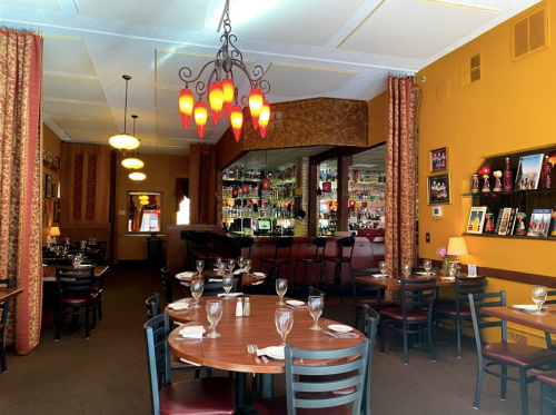 Cozy restaurant interior with wooden tables, elegant lighting, and a bar in the background. Warm colors and decor.