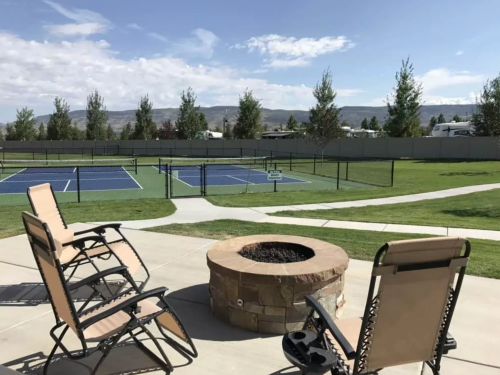 A view of a grassy area with two lounge chairs and a fire pit, overlooking tennis courts and distant mountains.