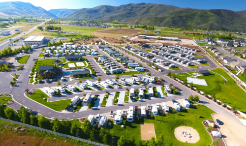 Aerial view of a large RV park with numerous parked RVs, surrounded by green hills and open fields.