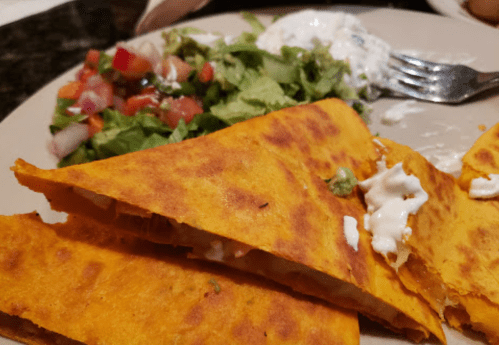 A plate with golden quesadillas, a side of fresh salad, and a dollop of sour cream.