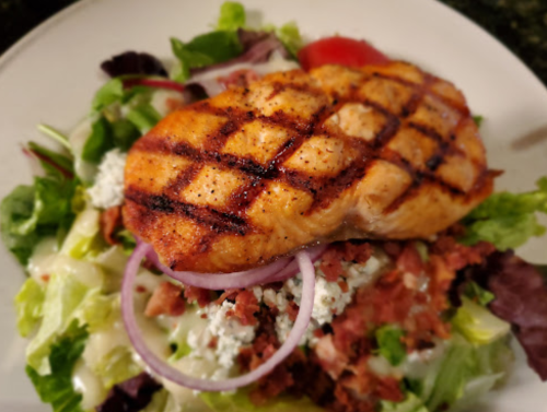 Grilled salmon fillet on a bed of mixed greens, topped with red onion and crumbled cheese.