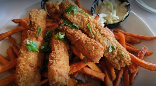 Crispy fried fish sticks served on a bed of sweet potato fries, garnished with green onions and a side of coleslaw.