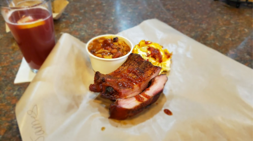 A plate with sliced barbecue meat, a side of baked beans, and a drink on a table.