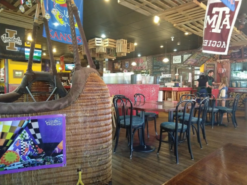 A cozy restaurant interior with wooden decor, empty tables, and colorful banners hanging from the ceiling.