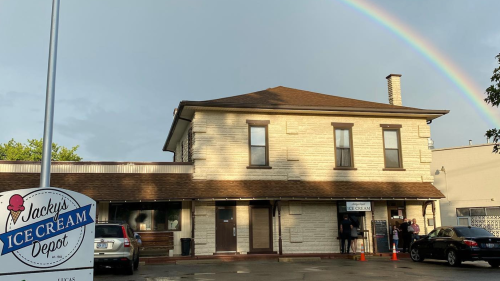 A charming ice cream shop with a rainbow in the sky, featuring a sign that reads "Jacky's Ice Cream Depot."