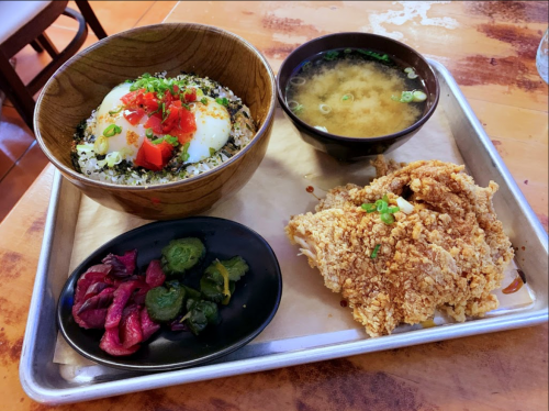 A tray with fried chicken, miso soup, rice topped with tomatoes, and pickled vegetables.