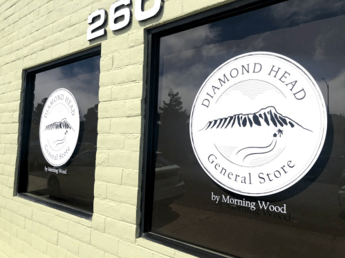 Two windows featuring the logo of "Diamond Head General Store by Morning Wood" on a green wall.