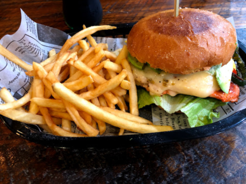 A burger with lettuce, tomato, and avocado, served with a side of golden fries on a black tray.