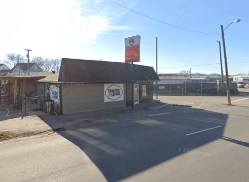 A small restaurant building with a sign reading "Burger Joint," located on a street with clear blue skies.