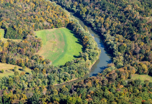 Aerial view of a winding river surrounded by vibrant autumn foliage and a green field.