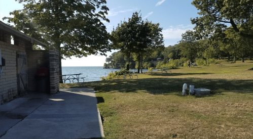 A serene lakeside park with trees, picnic tables, and a view of the water under a clear blue sky.