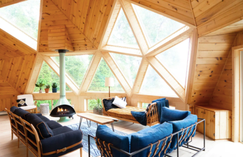 Cozy wooden living room with geometric windows, a fireplace, and stylish furniture, surrounded by greenery.
