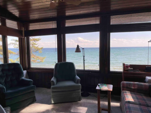 Cozy room with two chairs and a table, featuring large windows overlooking a serene lake and distant trees.