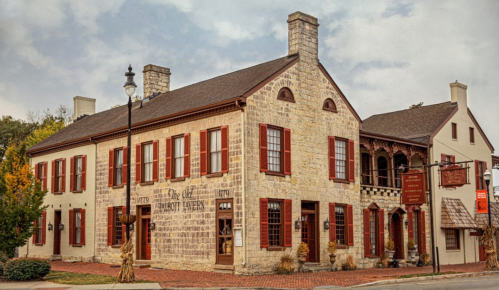 Historic stone building with red shutters, featuring a porch and signage for a tavern, set in a quaint town.