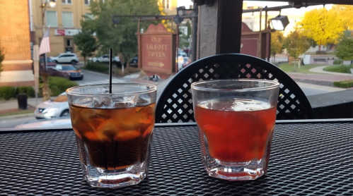 Two cocktails on a table with a view of a street and buildings in the background.