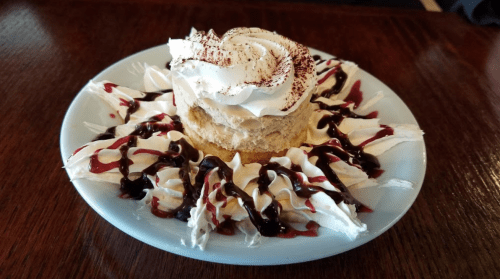 A dessert on a blue plate featuring a cake topped with whipped cream and drizzled with chocolate sauce.