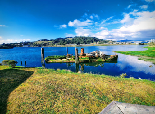 A scenic view of a calm river with an old, abandoned boat and lush green hills under a blue sky.