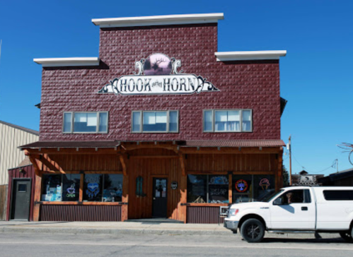 A two-story building with a maroon facade and a sign reading "Hook and Horn," featuring large windows and a white truck parked outside.