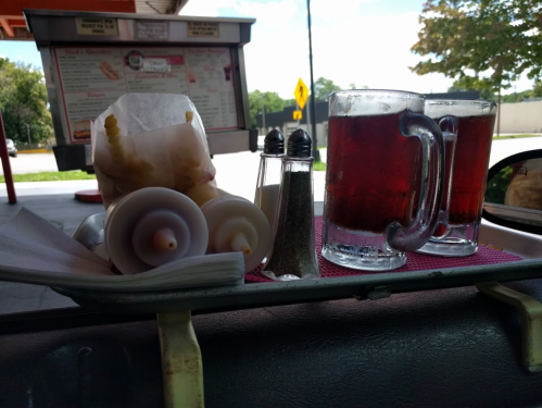 Two mugs of iced tea, a bag of popcorn, and salt and pepper shakers on a tray at a drive-in restaurant.