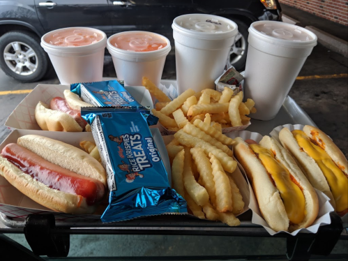 A tray with hot dogs, crinkle-cut fries, and Rice Krispies Treats, alongside four cups of drinks.