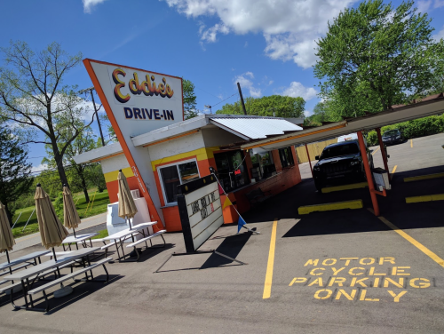 A colorful drive-in restaurant with outdoor seating and a sign reading "Eddie's Drive-In," featuring motorcycle parking.