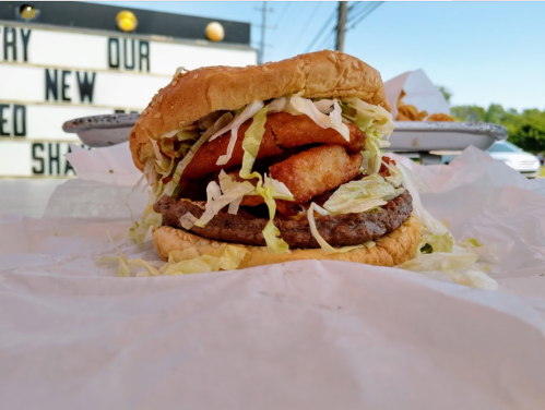 A close-up of a burger with lettuce, onion rings, and a beef patty, set on a table with a blurred background.
