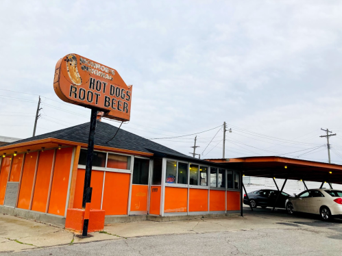 A retro-style restaurant with an orange exterior, featuring a sign that reads "Monroe's Hot Dogs Root Beer."
