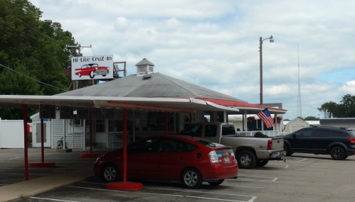 A diner with a red and white awning, featuring a sign with a vintage car and an American flag in front.