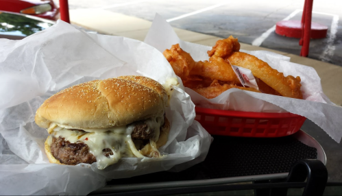 A cheeseburger with melted cheese and grilled onions next to a basket of crispy onion rings.