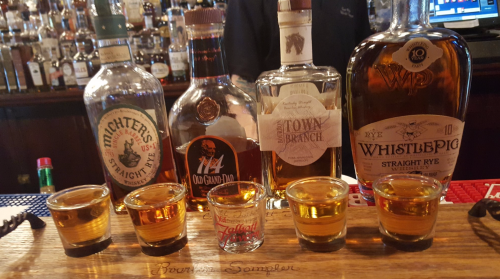 A selection of whiskey bottles and shot glasses filled with whiskey on a bar counter.