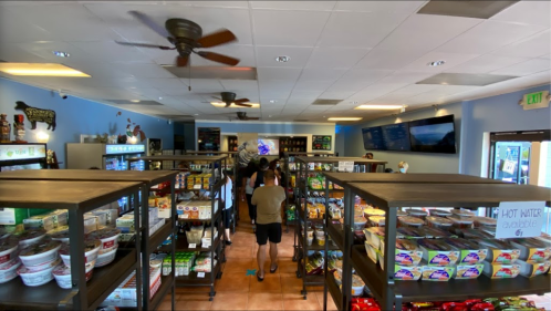 A view of a grocery store interior with shelves stocked with various food items and customers browsing.